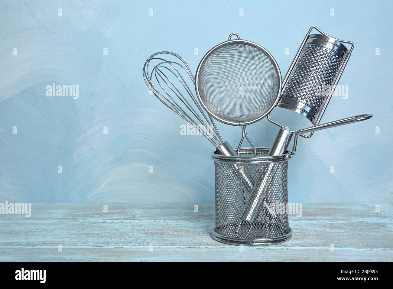 Kitchen utensils in deep fry basket on table against blue wall Stock