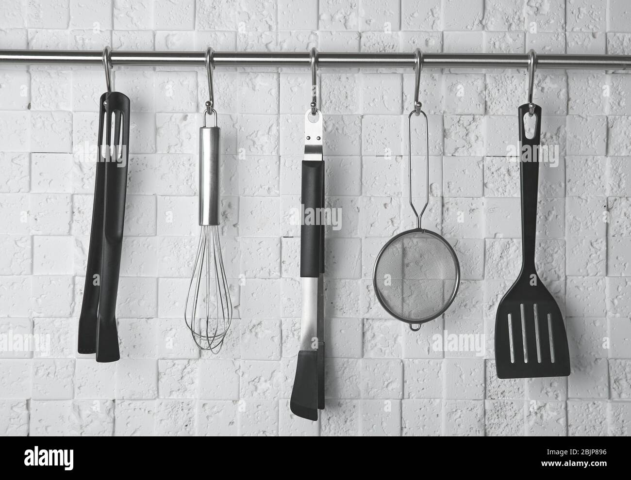 Kitchen utensils hanging on rack against white wall Stock Photo