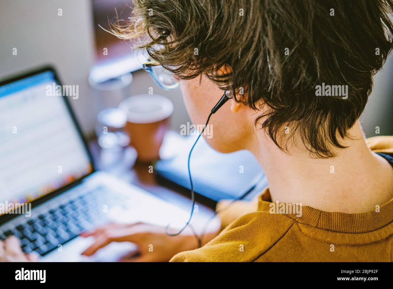 Woman working on desk in home office in old vintage room. Young Caucasian short hair woman with earphones working online from home on computer laptop Stock Photo