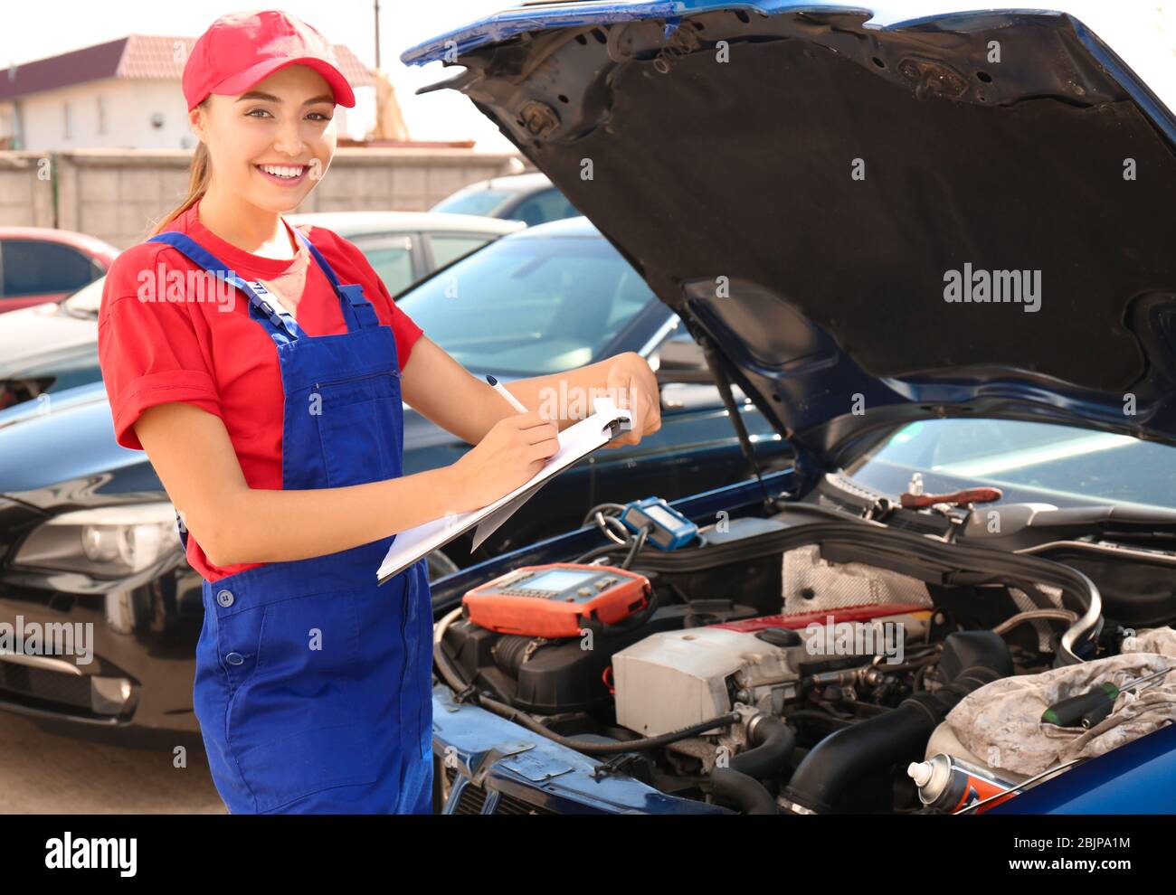 Young female mechanic with clipboard near car in body shop Stock Photo