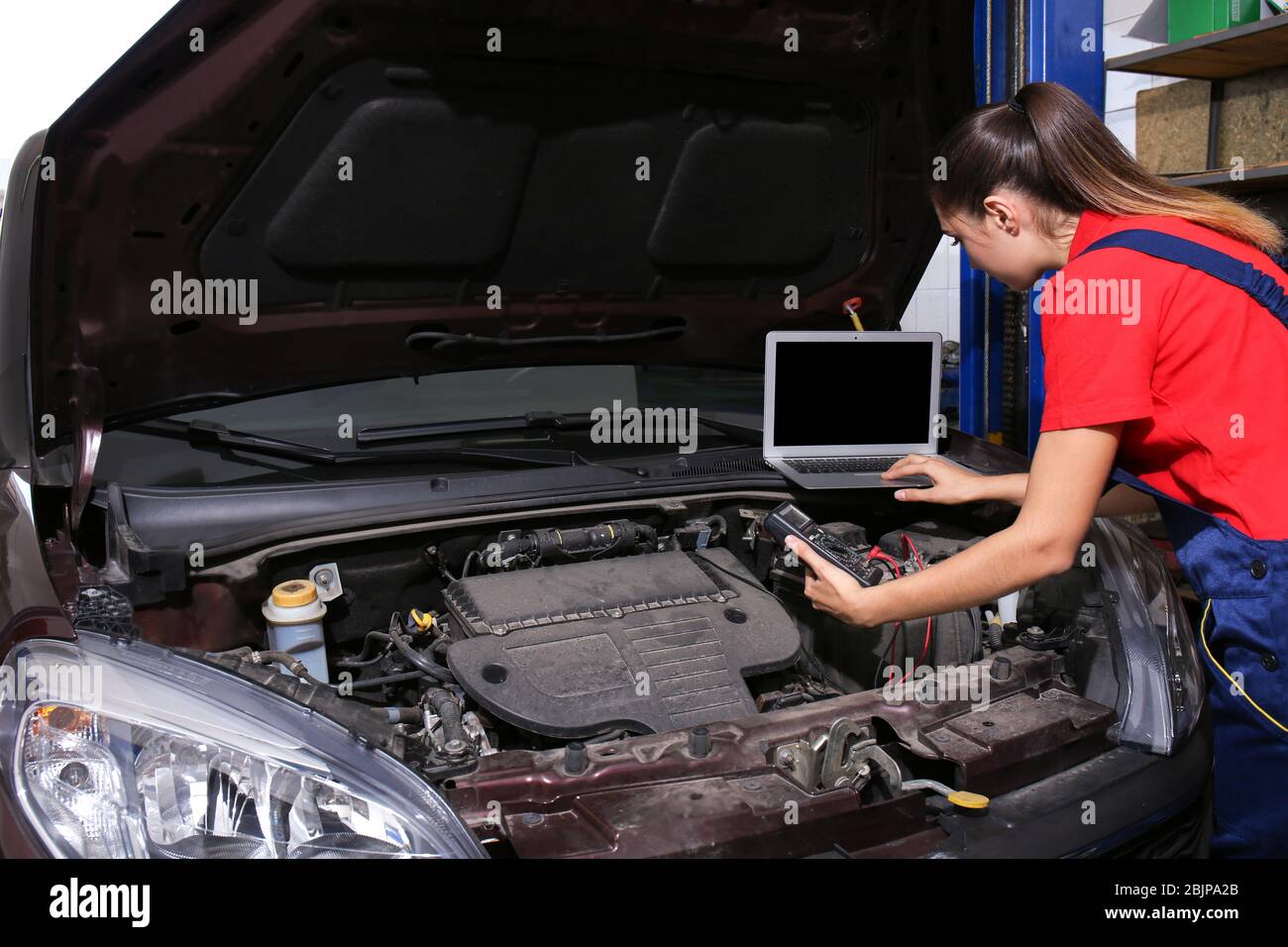 Young female mechanic with laptop repairing car in body shop Stock Photo