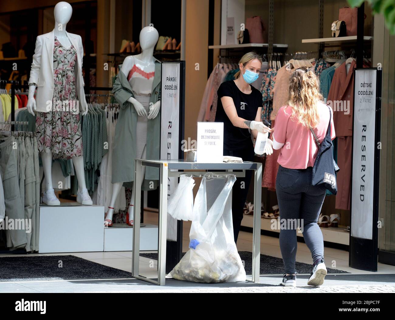Prague, Czech Republic. 30th Apr, 2020. An employee, left, of Reserved clothing store helps a customer with hand disinfection at the entrance to the store, on April 30, 2020, in Prague, Czech Republic. The shops reopened on April 27 after a forced break due to coronavirus, but increased hygiene measures are in place. Credit: Katerina Sulova/CTK Photo/Alamy Live News Stock Photo