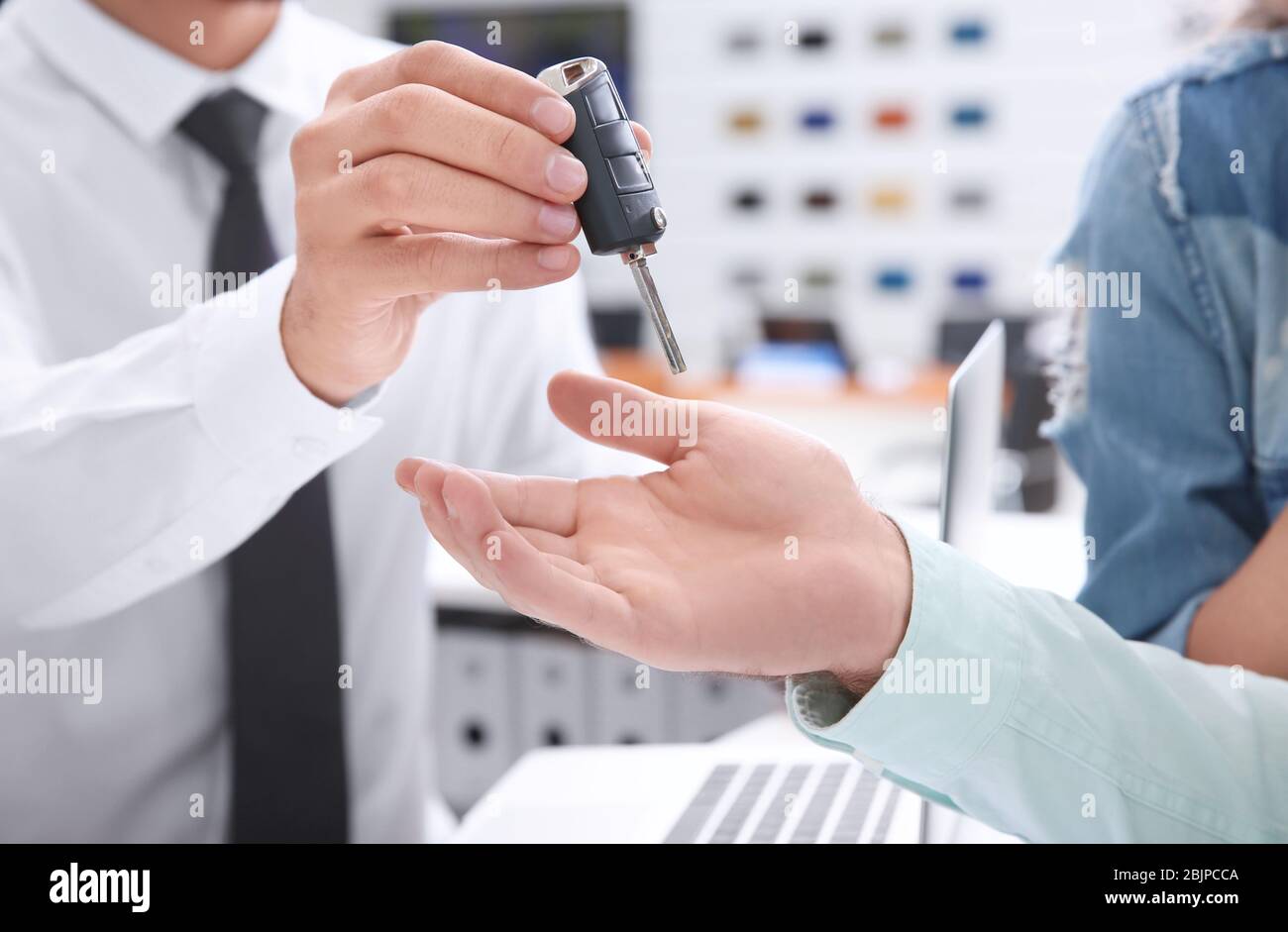 Car salesman giving key to couple in dealership Stock Photo - Alamy