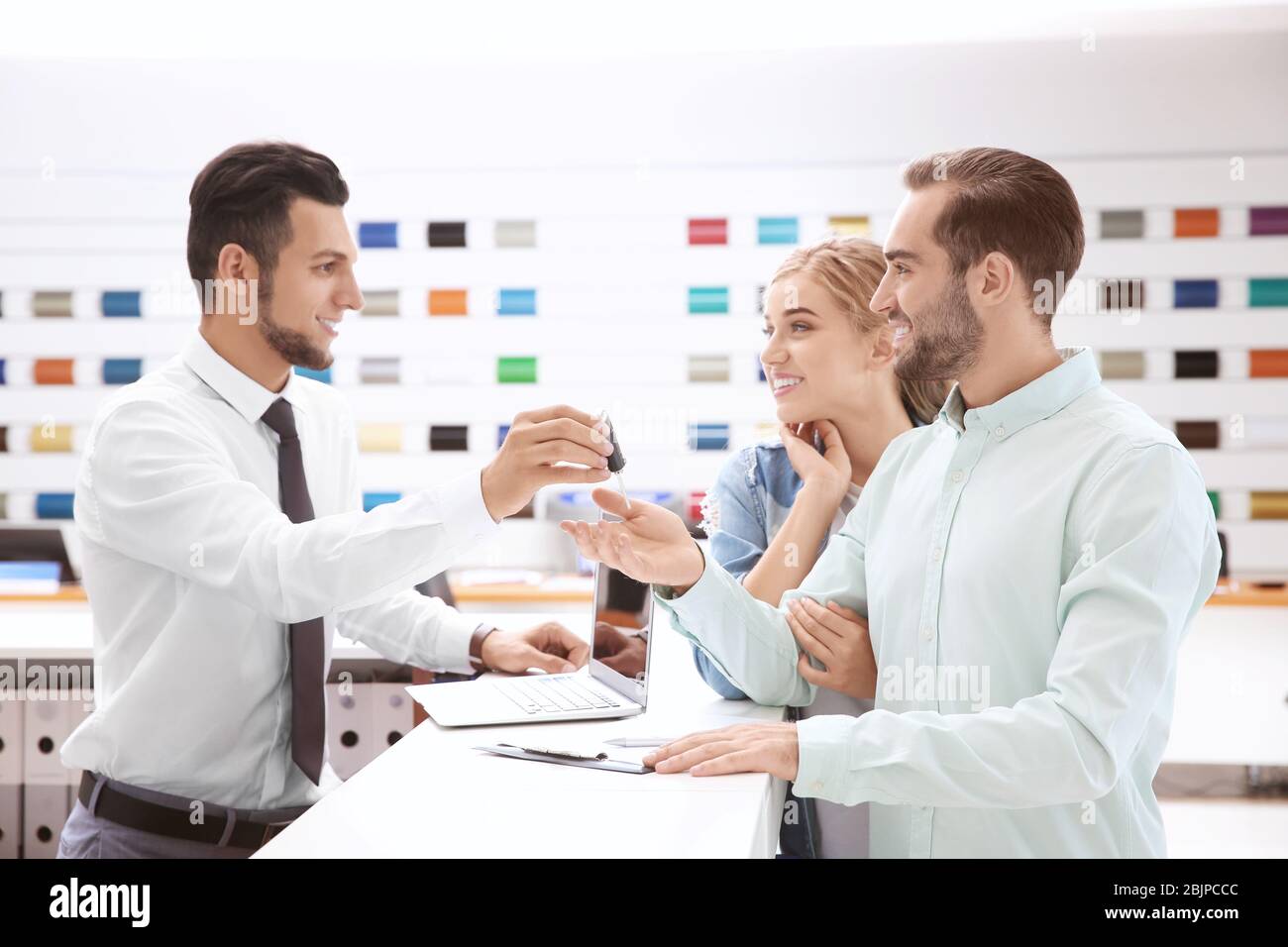 Car salesman giving key to couple in dealership Stock Photo - Alamy
