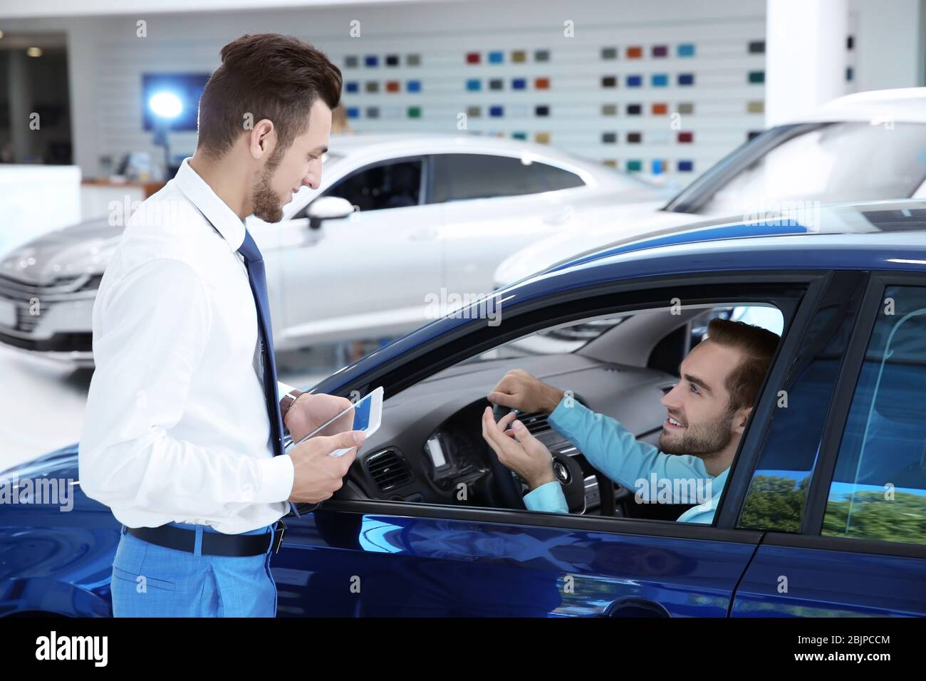 Man sitting on driver's seat while talking to car salesman Stock Photo