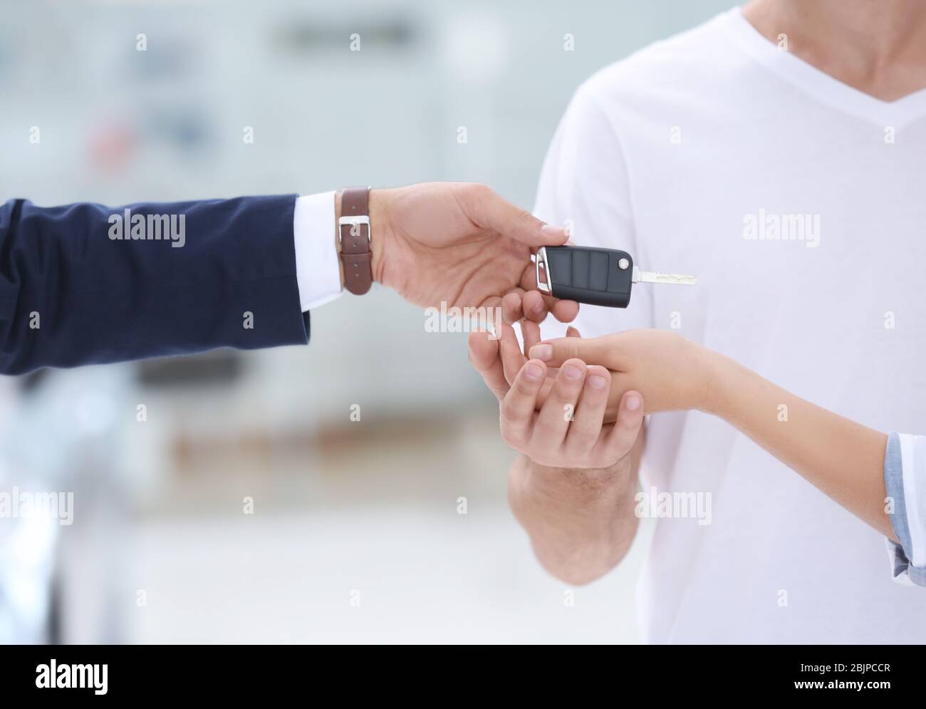 Car salesman giving key to couple in dealership Stock Photo - Alamy
