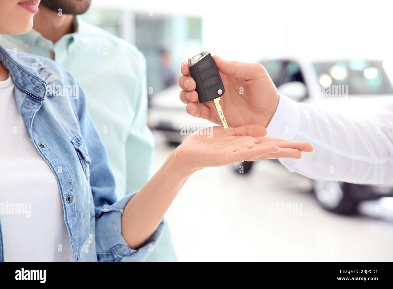 Car salesman giving key to couple in dealership Stock Photo - Alamy