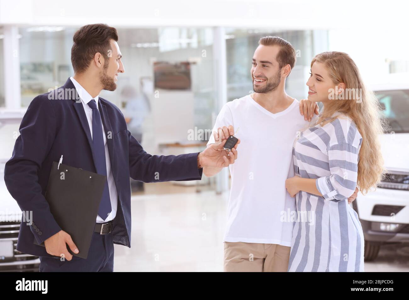 Car salesman giving key to couple in dealership Stock Photo - Alamy