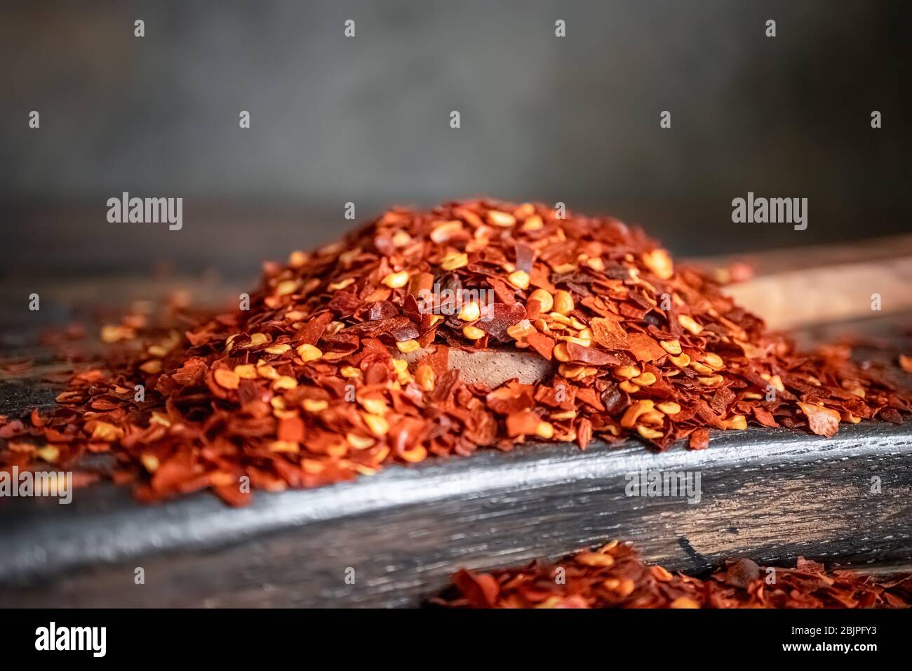 Flakes of red hot chili pepper in wooden spoon closeup on a kitchen table. Stock Photo