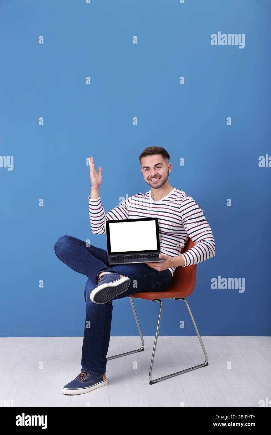Young man with laptop against blue wall Stock Photo - Alamy