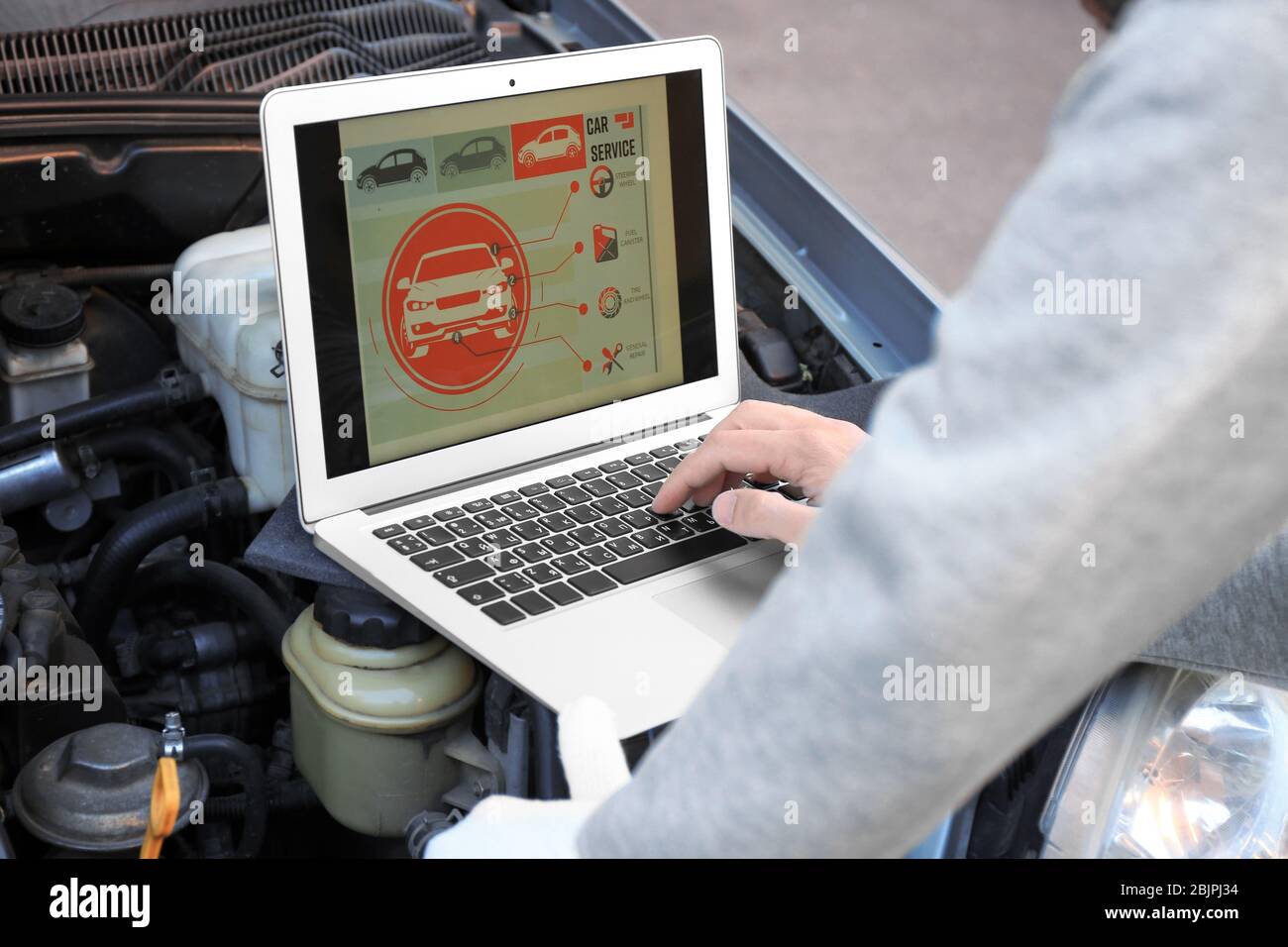 Young male mechanic using computer diagnostic while repairing car Stock Photo