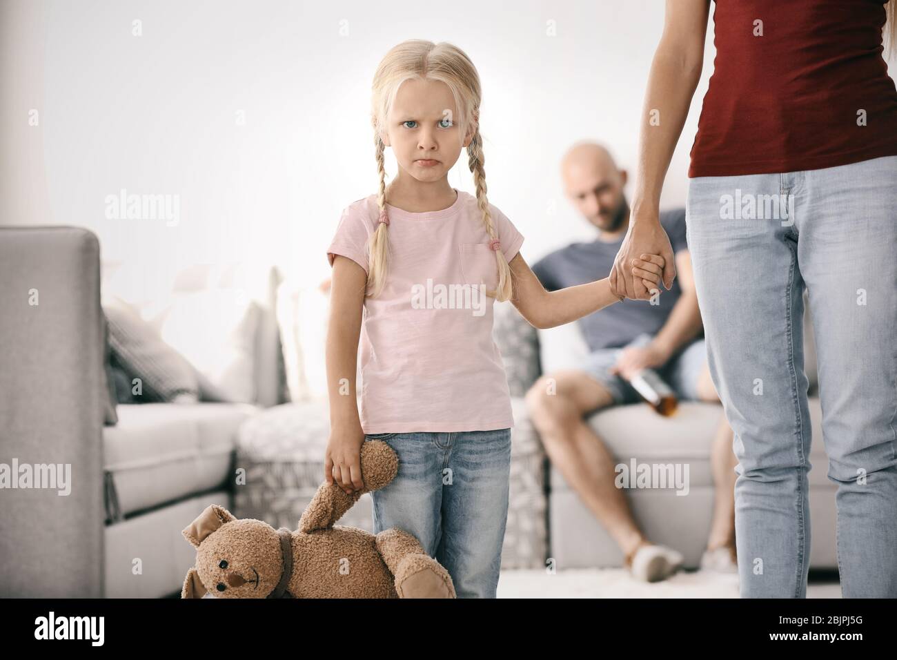 Young woman and little girl with blurred drunk man at home Stock Photo