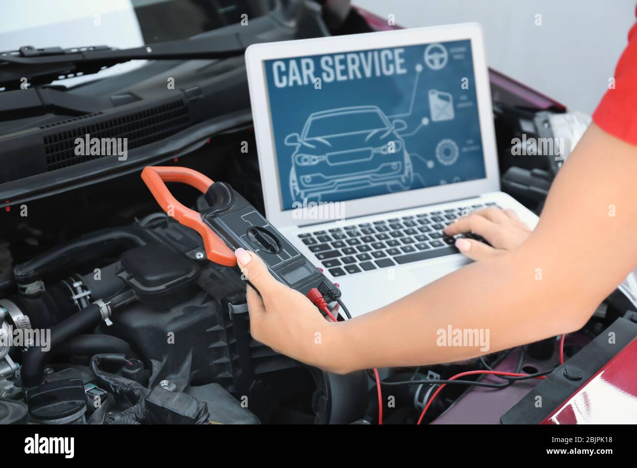 Young female mechanic with laptop repairing car in body shop Stock Photo