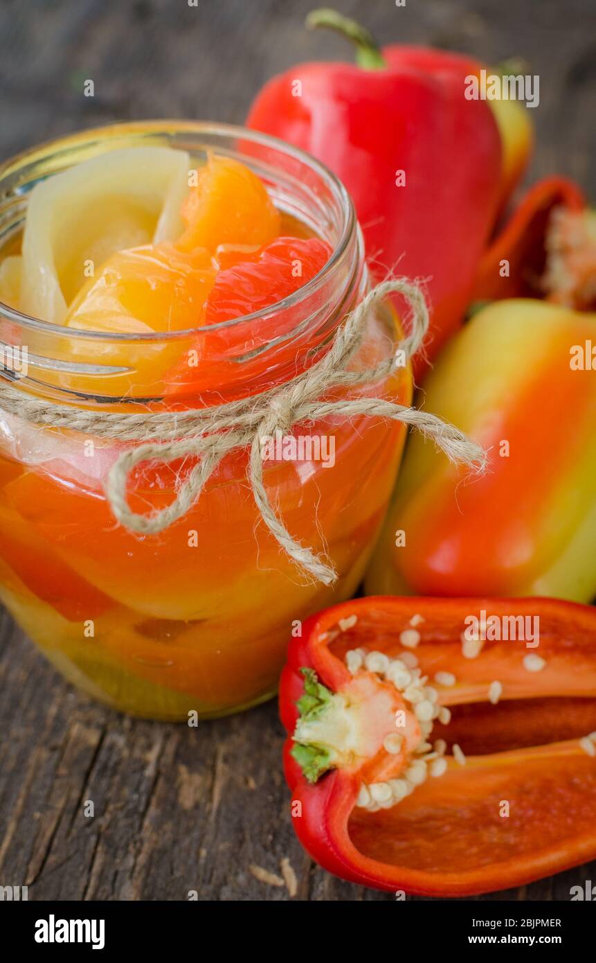 Bell pepper preserved in a glass jar with fresh peppers on old wooden background. Homemade