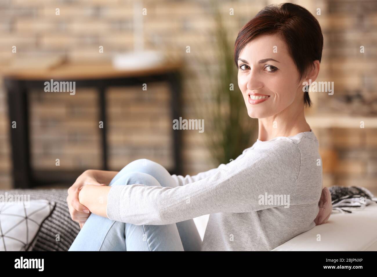 Beautiful mature woman sitting on sofa at home Stock Photo - Alamy