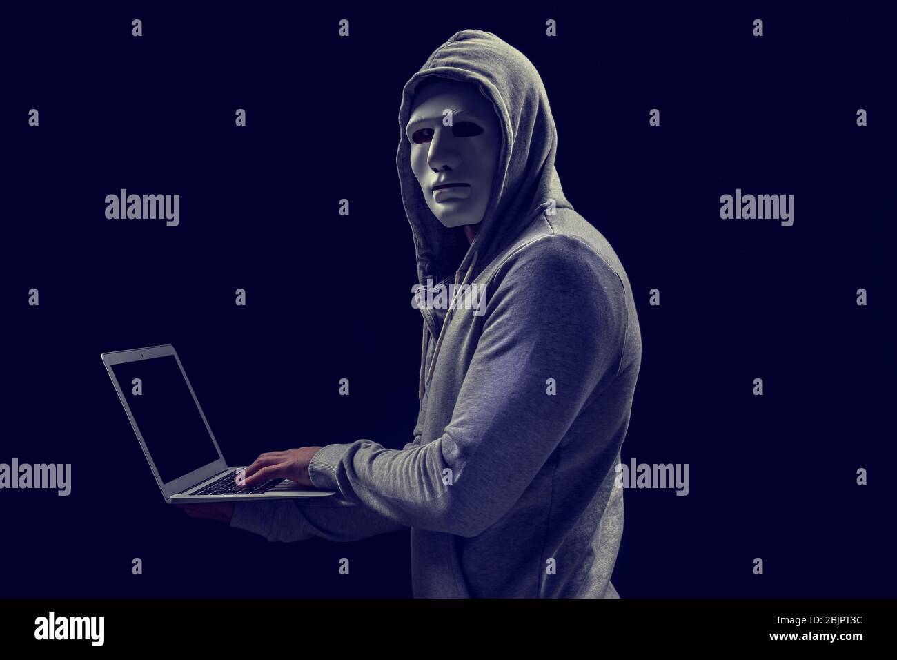 Hacker in mask with laptop on dark background Stock Photo - Alamy