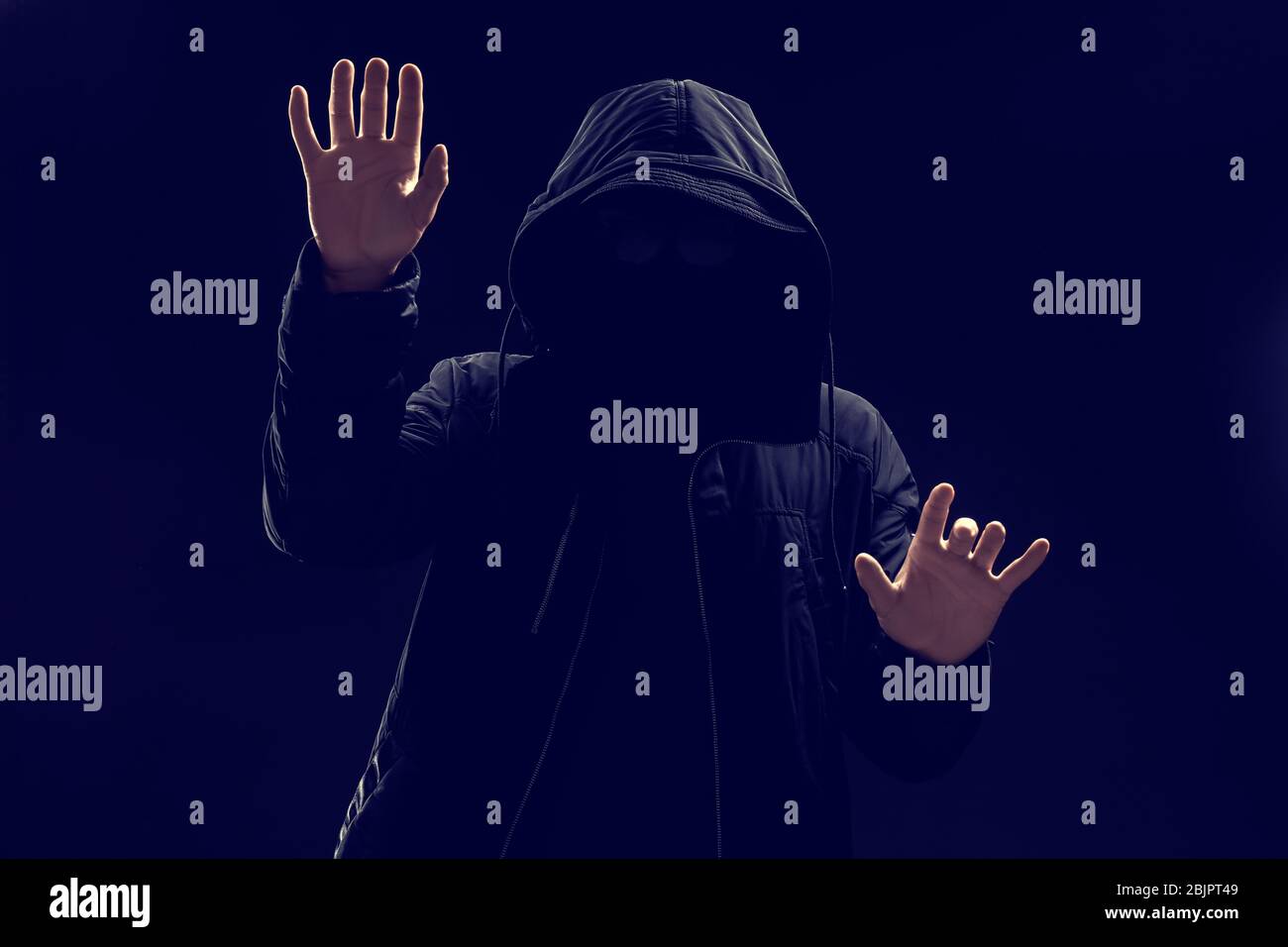Hacker in hood working with virtual screen on dark background Stock Photo