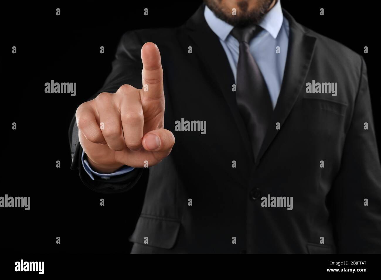 Businessman pushing button on virtual screen against dark background Stock Photo