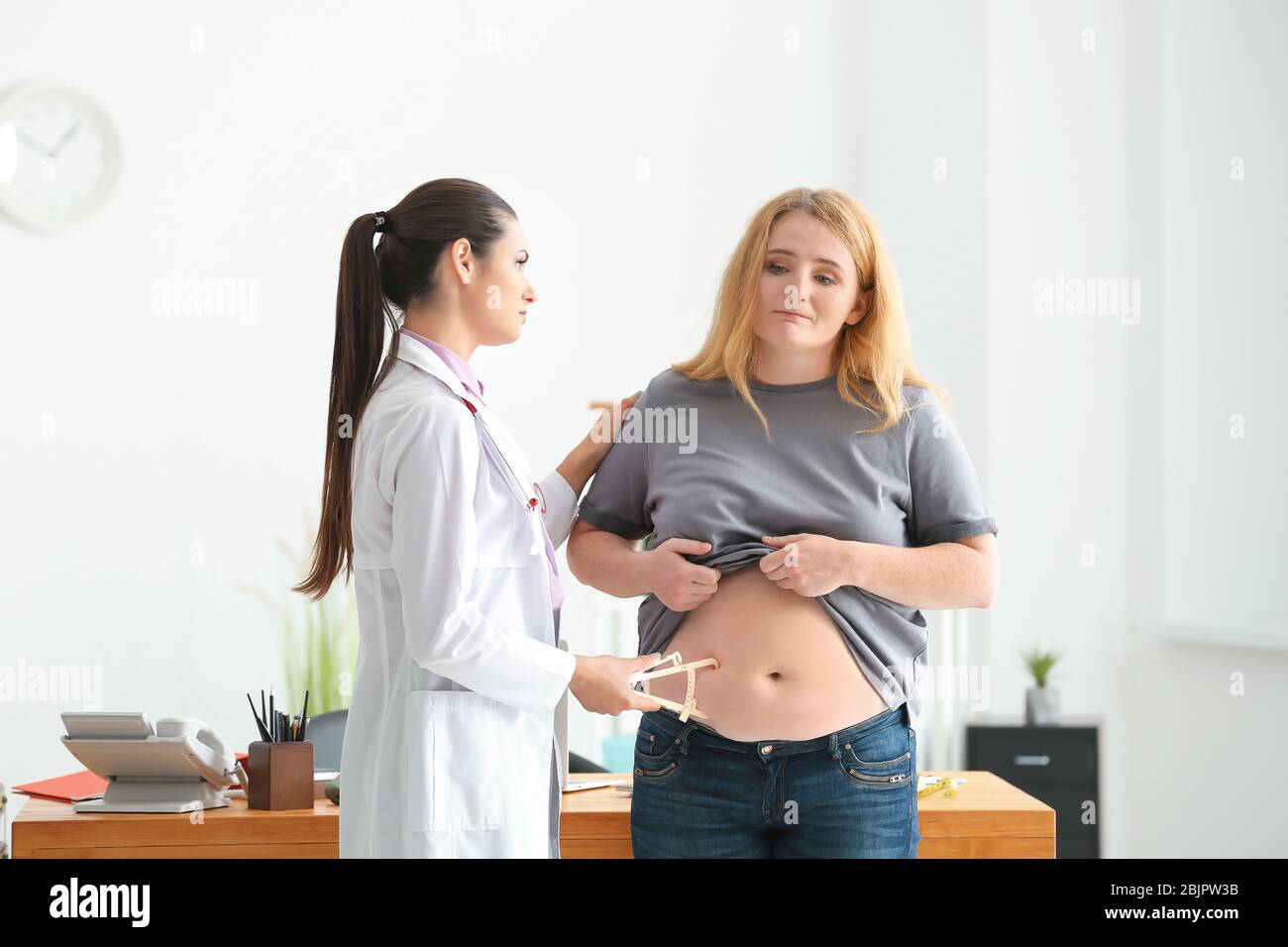 Young female doctor measuring fat layer of overweight woman with caliper in clinic Stock Photo