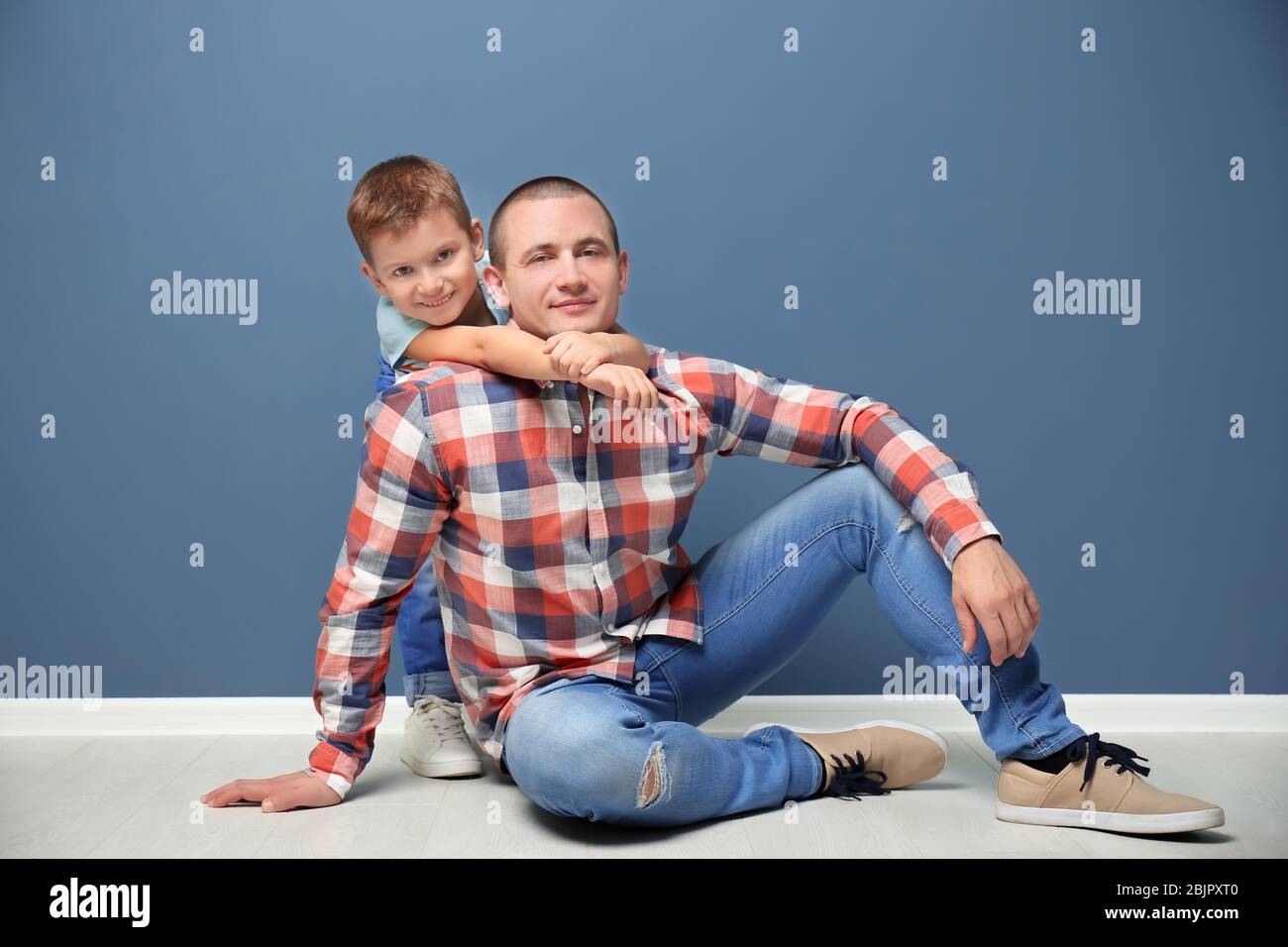 Dad and his son sitting on floor near color wall Stock Photo - Alamy
