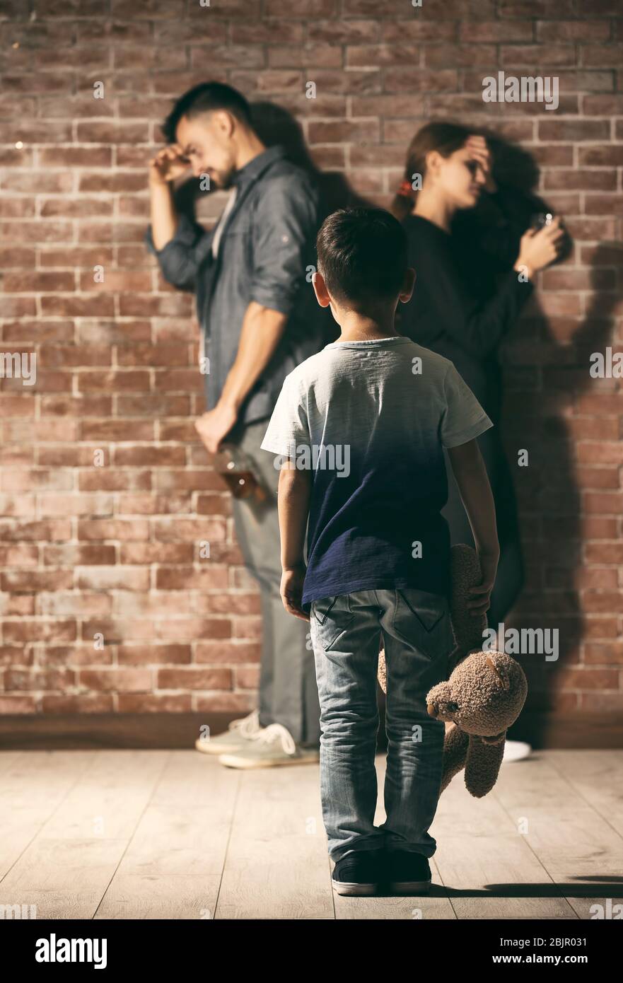 Little boy holding teddy bear while his parents having quarrel on background Stock Photo