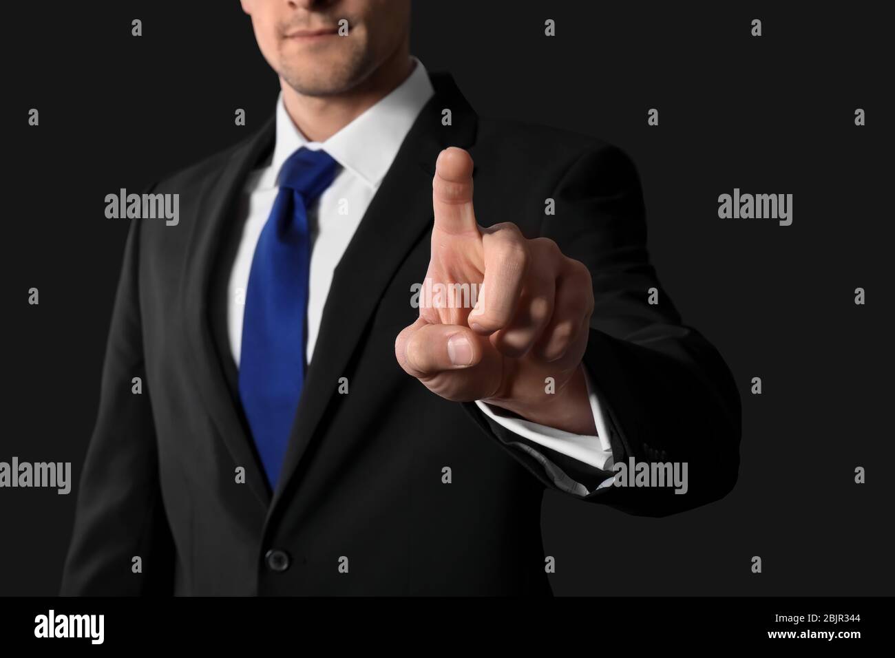 Businessman pushing button on virtual screen against dark background Stock Photo
