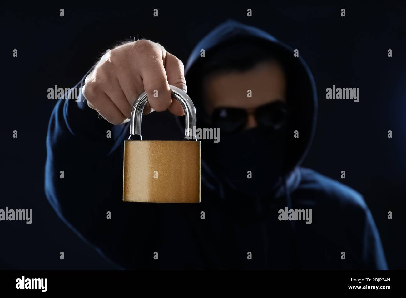 Hacker in mask holding lock on dark background Stock Photo