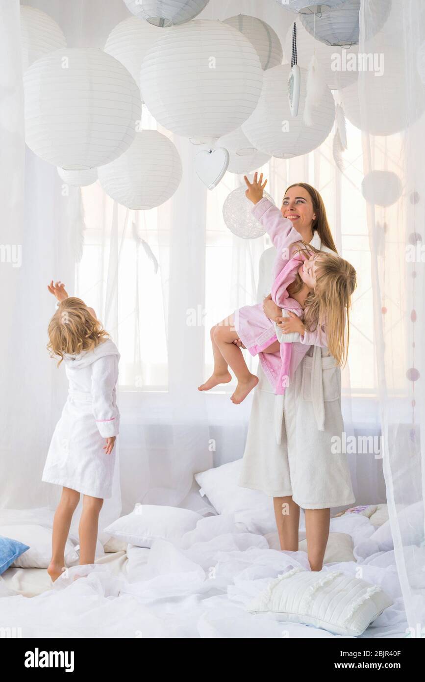 Young woman playing on the bed with the two daughters at home. Stay home and family concept. Stock Photo