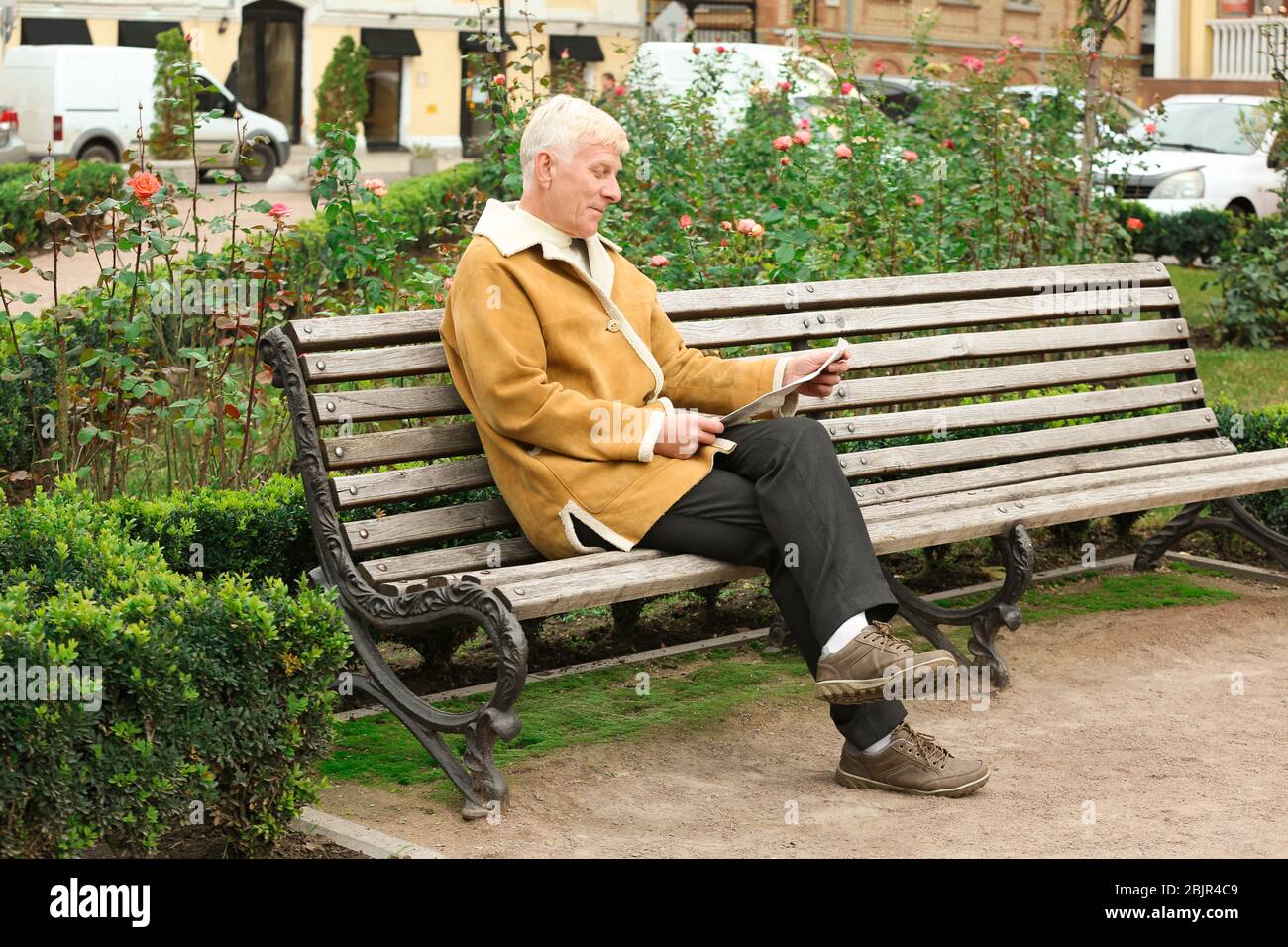 Handsome mature man reading newspaper on bench outdoors Stock Photo - Alamy