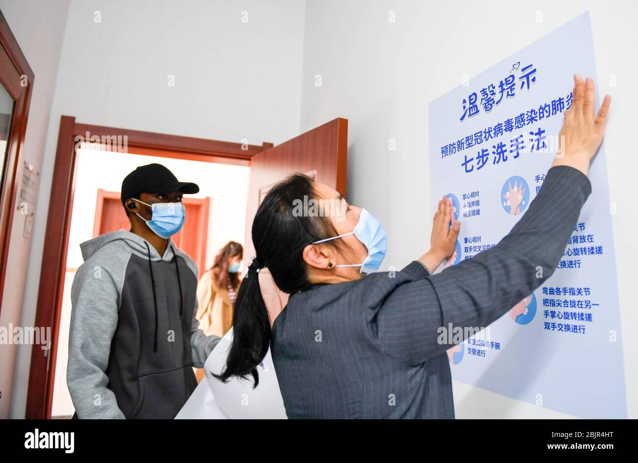 (200430) -- CHANGCHUN, April 30, 2020 (Xinhua) -- Mustapha (L) helps a teacher to post anti-epidemic poster in Changchun University of Chinese Medicine in Changchun, northeast China's Jilin Province, April 27, 2020. Mustapha Abdul Raheem has experienced two epidemics in the past six years: one was the Ebola in West Africa in 2014, during which he witnessed sufferings and aspired to study medicine; the other was the COVID-19. This time as a medical student in China, he was better prepared, both professionally and mentally. TO GO WITH 'Feature: An African medical student's fight against COVID-19 Stock Photo