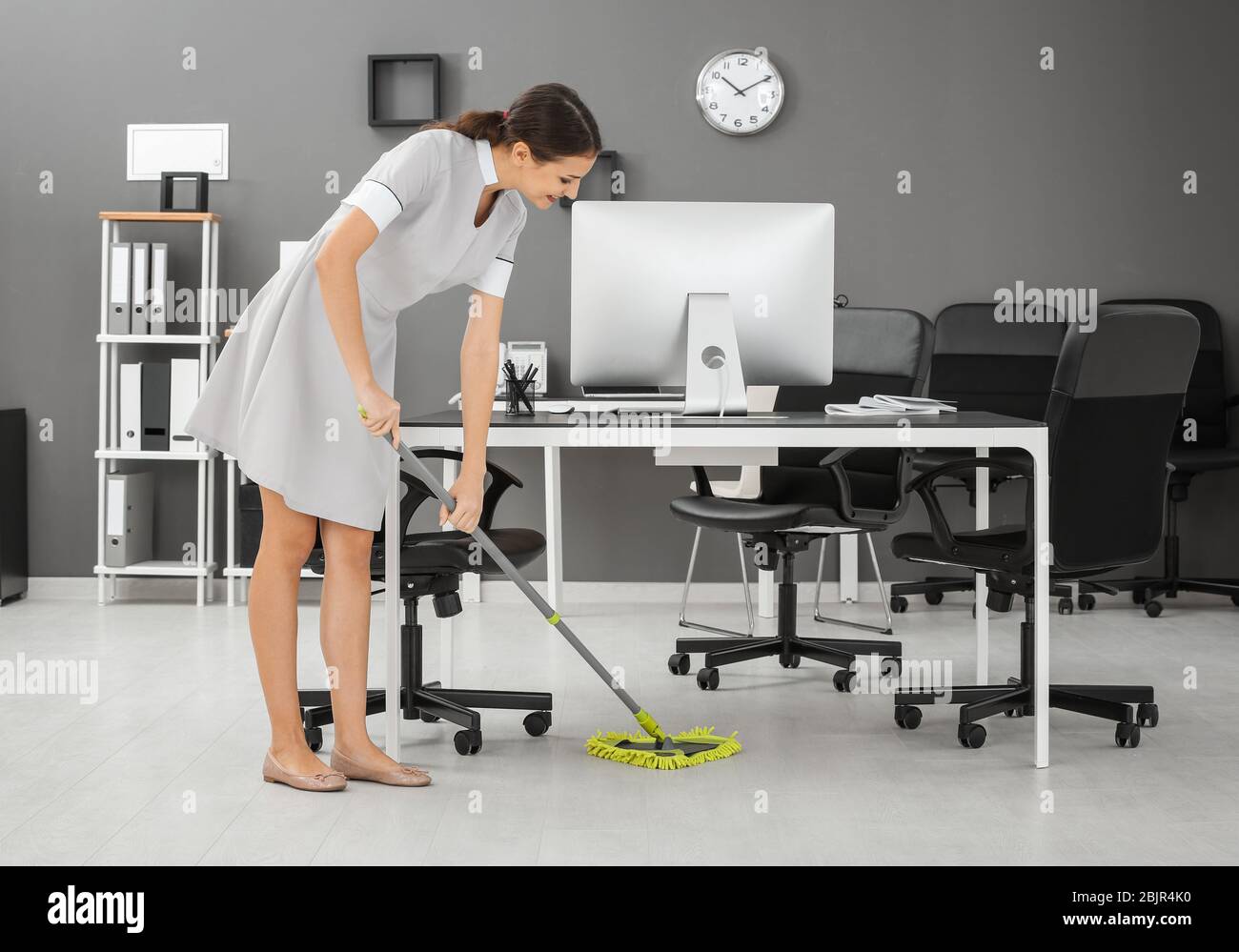Young woman mopping floor in office Stock Photo