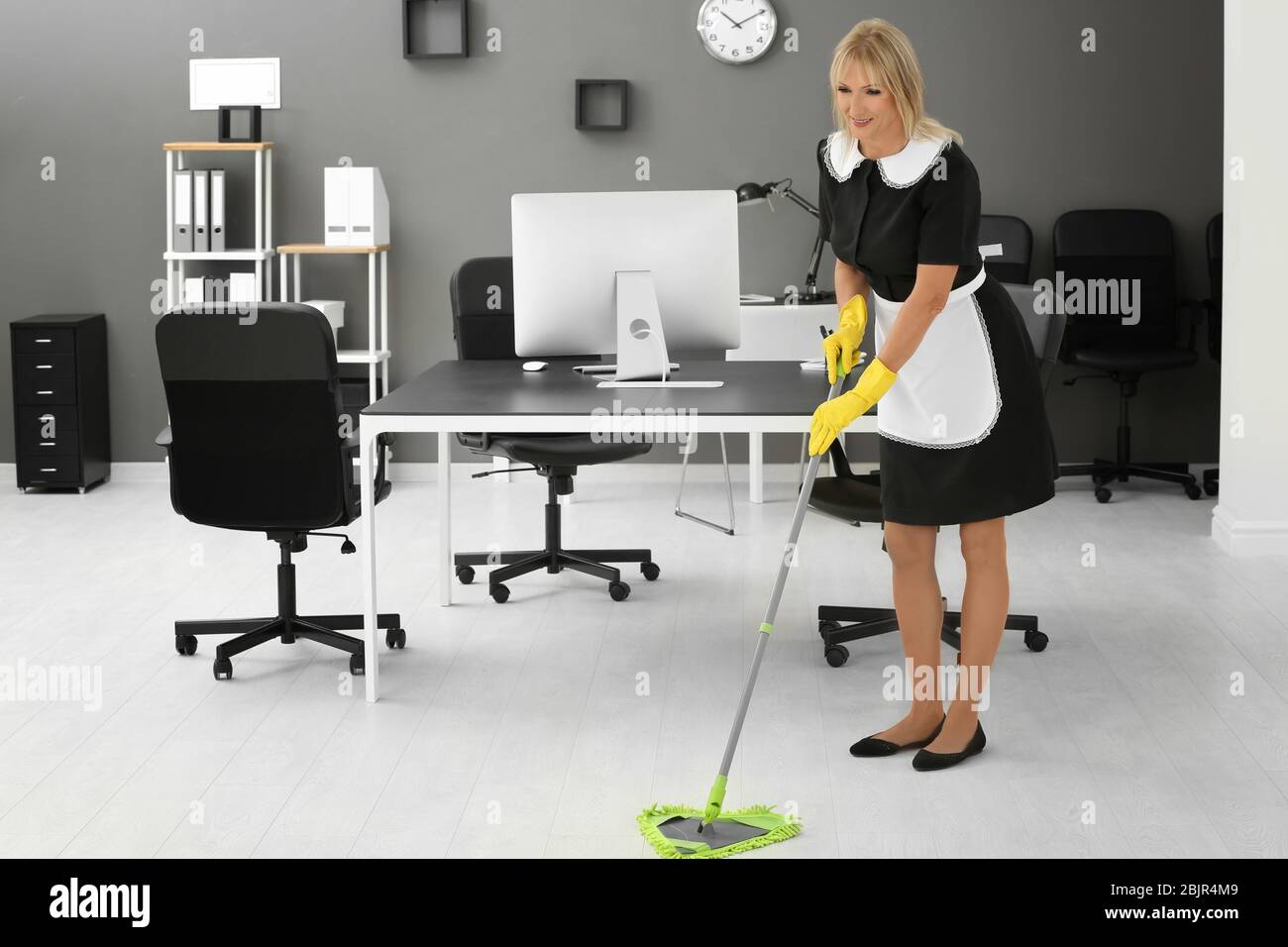 Mature charwoman mopping floor in office Stock Photo