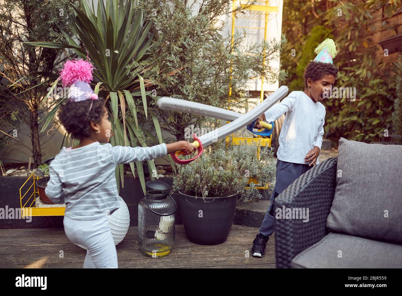 Afro-American boy and girl playing in the backyard with plastic swords, active Stock Photo