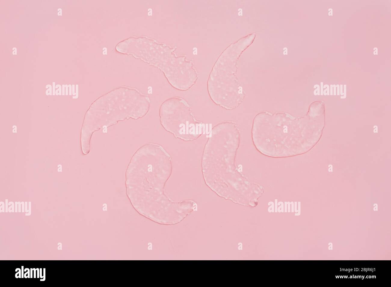 Squeezed cosmetic clear cream gel texture. Close up photo of transparent drop of skin care product. High Quality transparent gel with bubbles closeup on pink background. Stock Photo