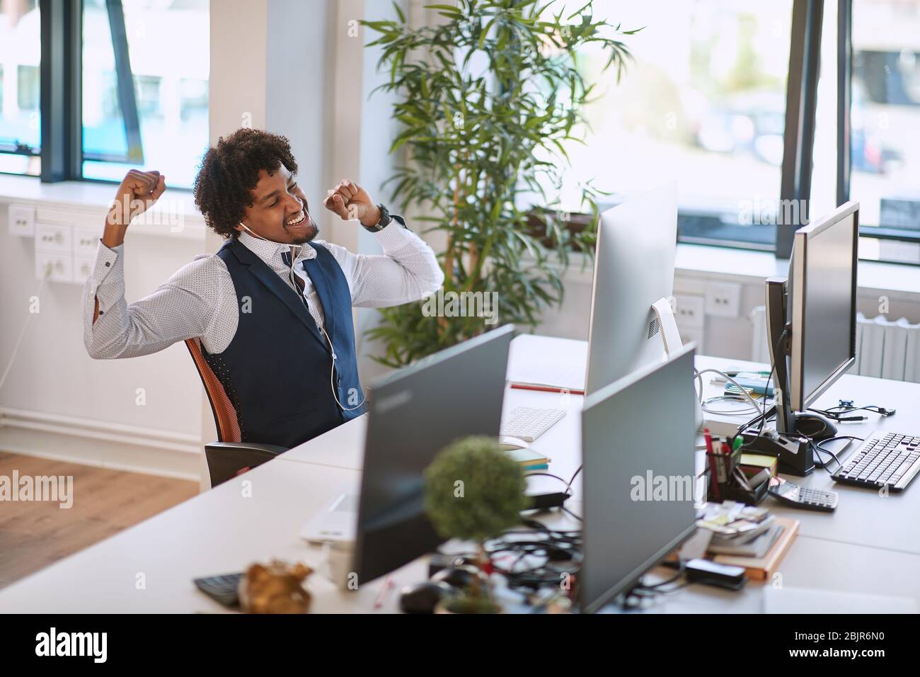 young afro-american business man stretches contentedly at his workplace in his office after receiving a good news Stock Photo