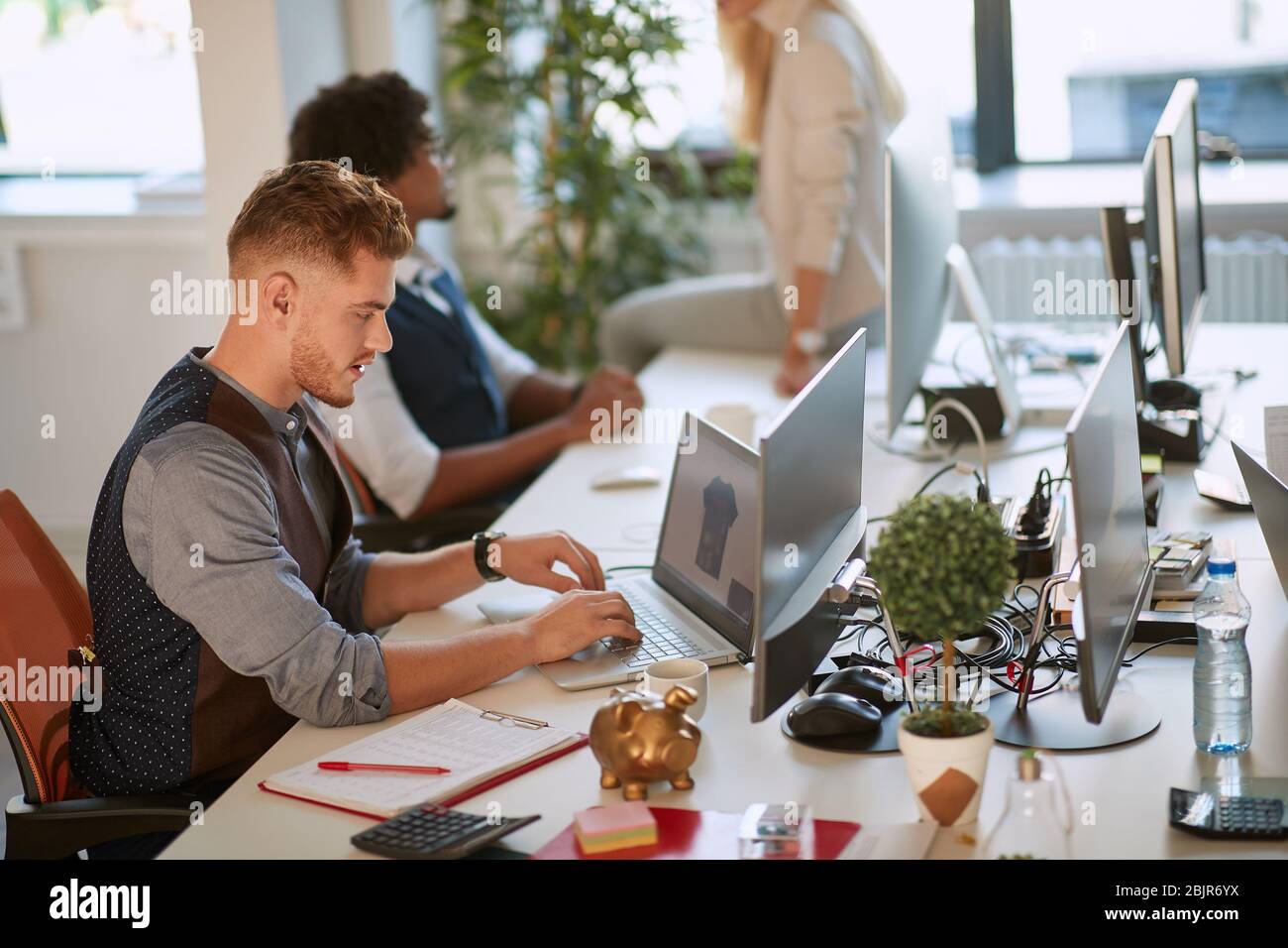 young designer typing on computer keyboard at workplace in the open ...