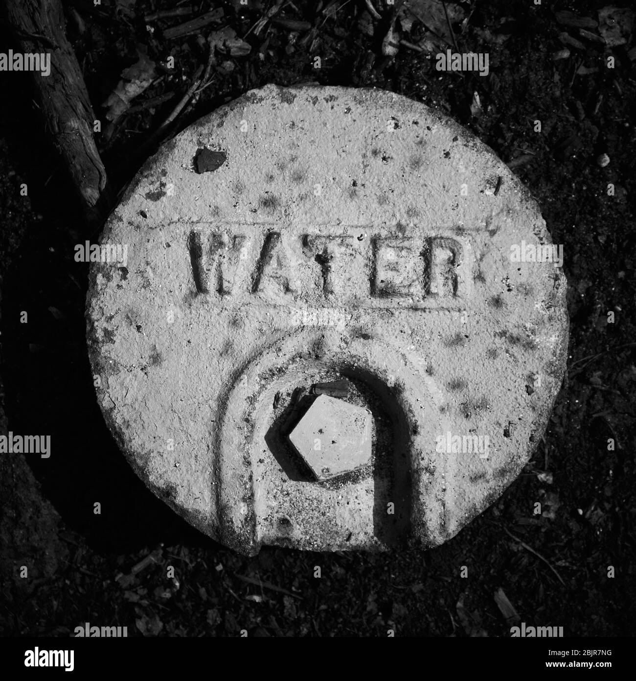 B&W photo of round cover of municipal water supply to residential or commercial establishment, covering below ground shut off valve. Stock Photo