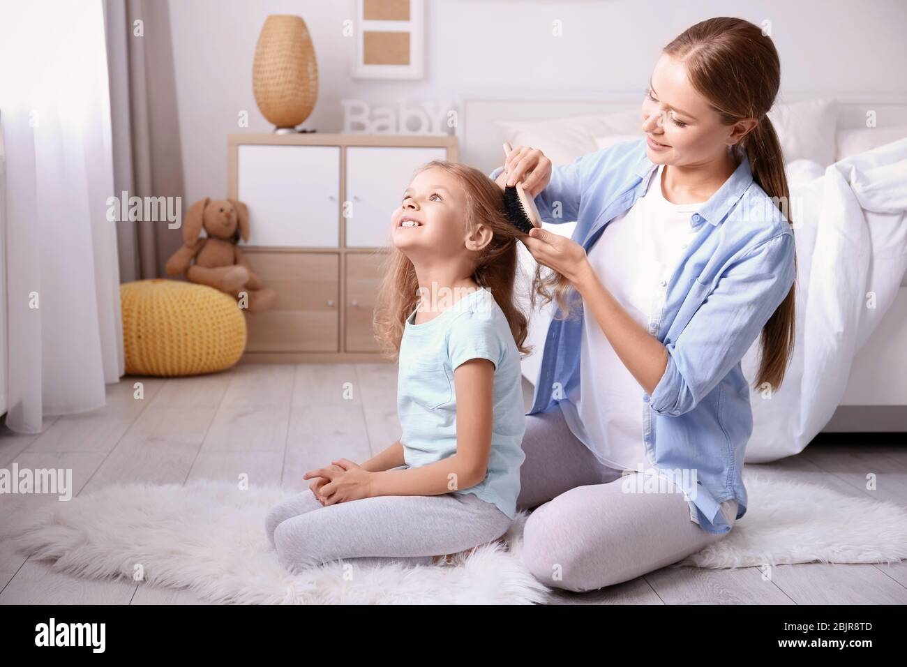 Happy mother combing daughter's hair in children room Stock Photo