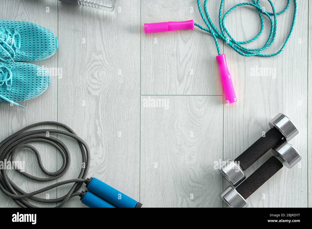Jumping ropes, dumbbells and sneakers on wooden background, top view Stock Photo