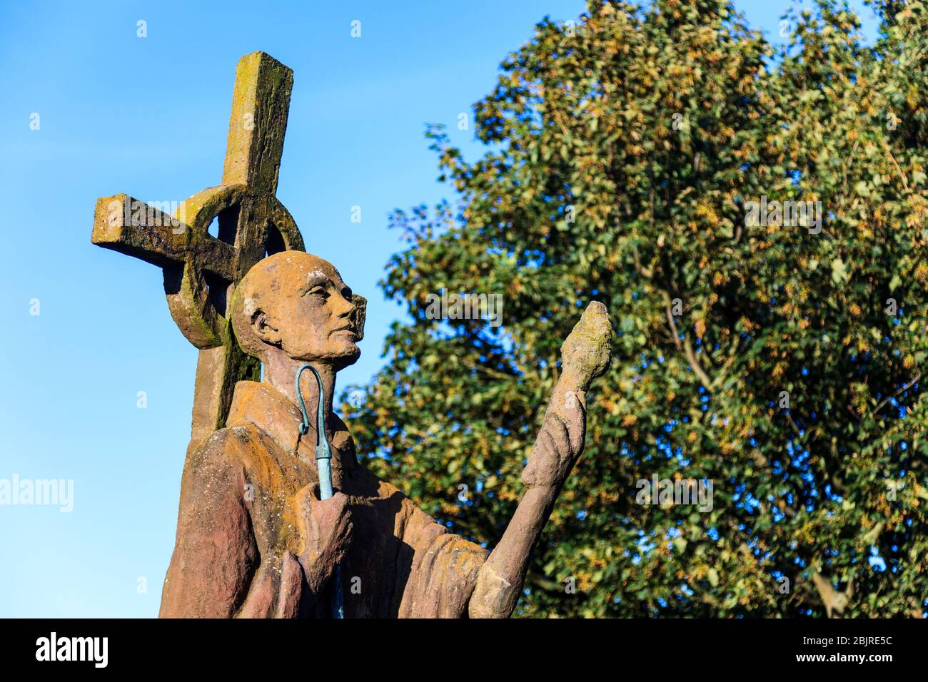 A modern statue of St Aidan of Lindisfarne next to the ruined Priory on Holy Island, Northumberland, England Stock Photo