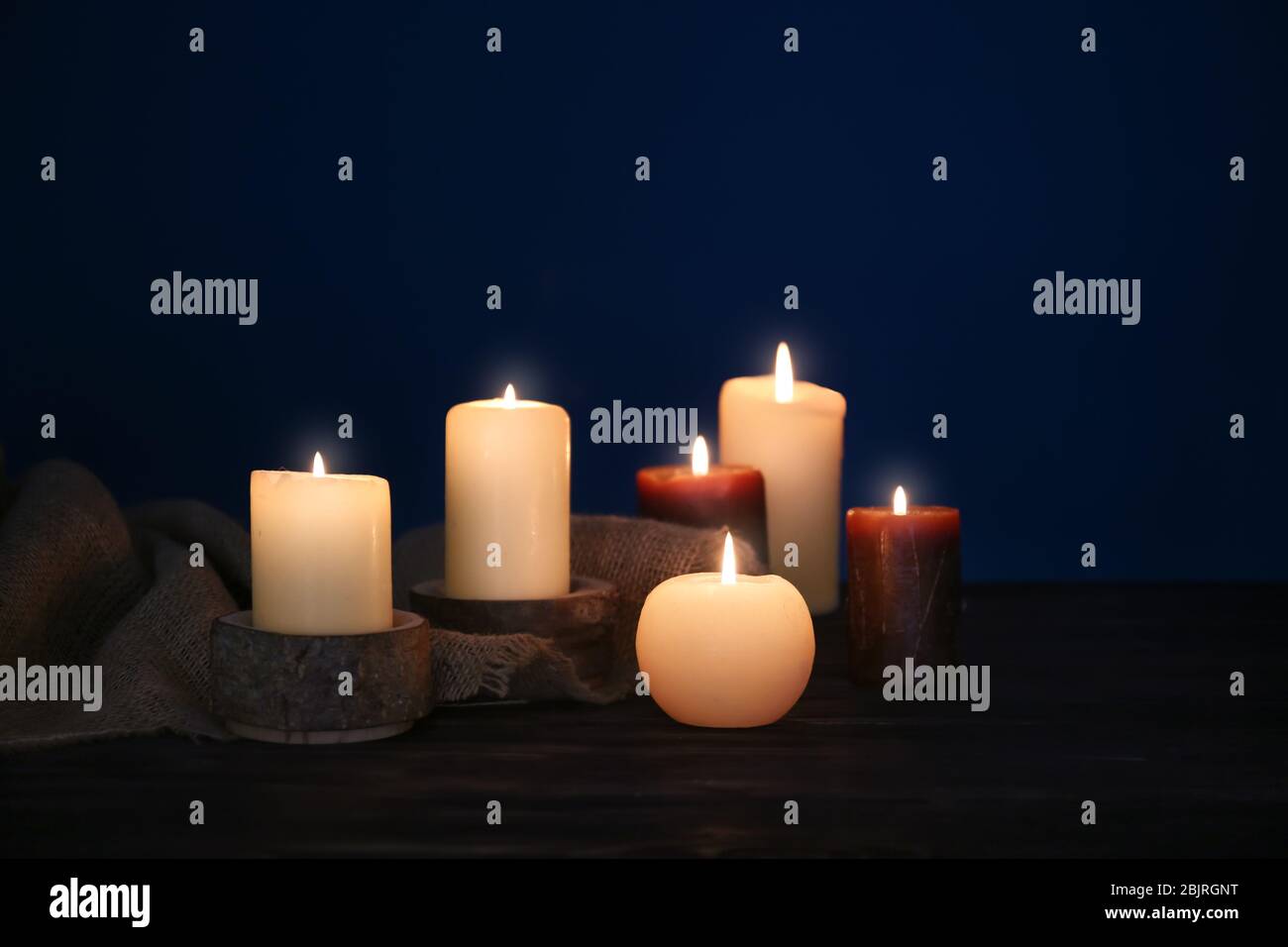 Burning candles on table against dark background Stock Photo - Alamy