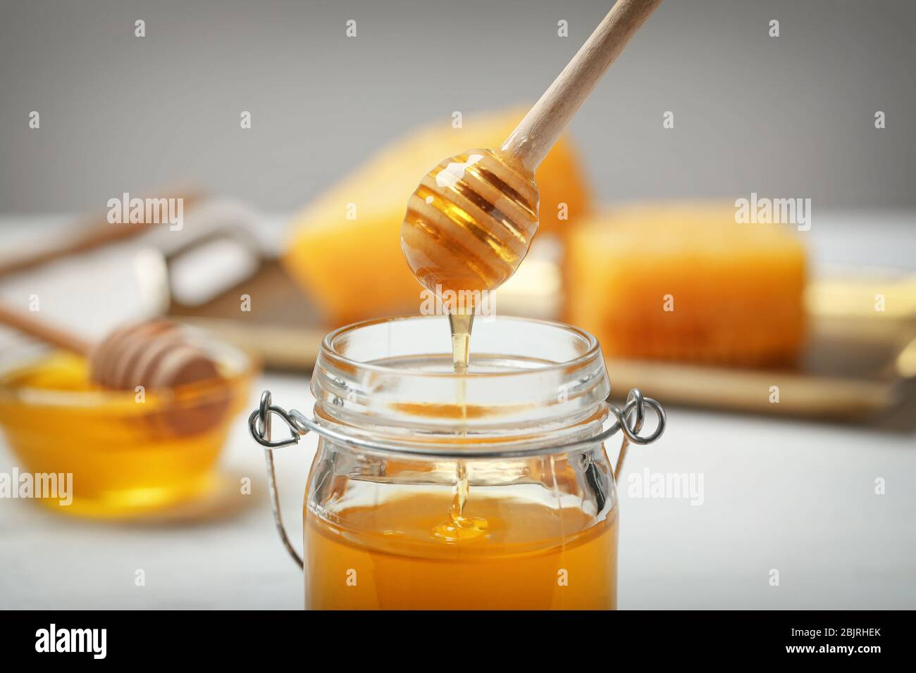 Honey dripping from wooden dipper into jar on blurred background ...