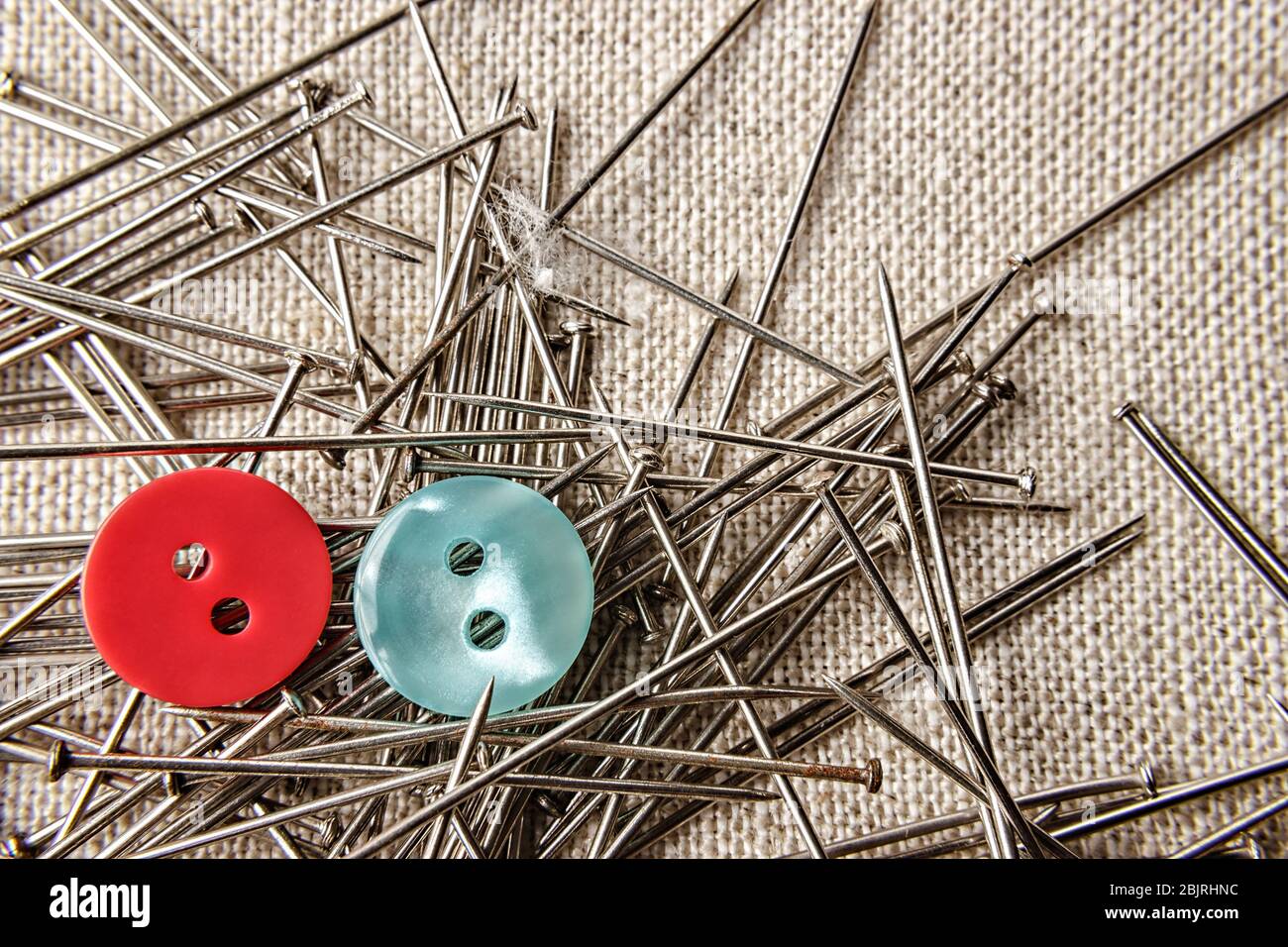 Red and blue button with seamstress pins on sack clothes. Close up. Stock Photo