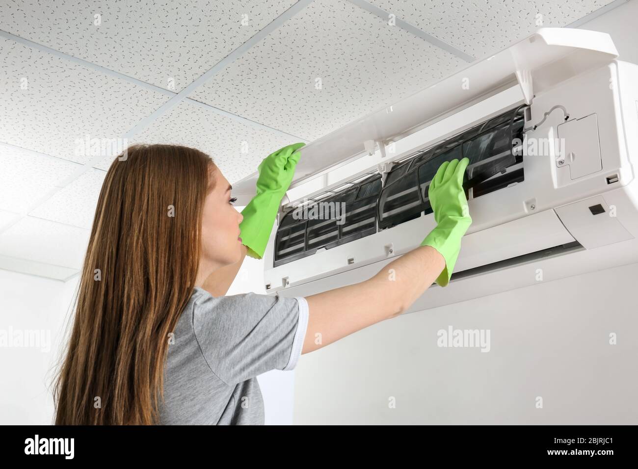 Young woman cleaning air conditioner, indoors Stock Photo