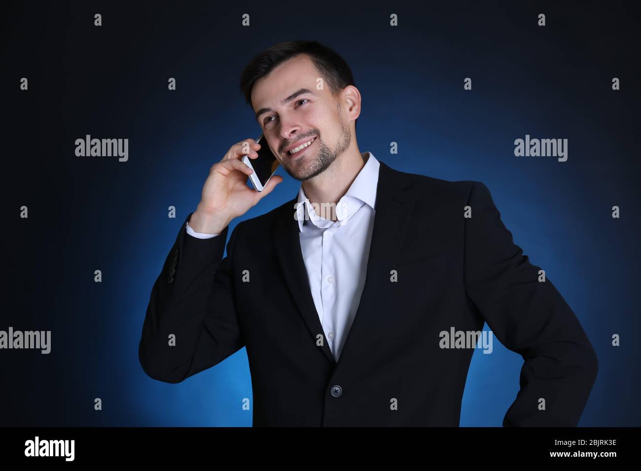 Man in formal suit talking on phone against dark background Stock Photo
