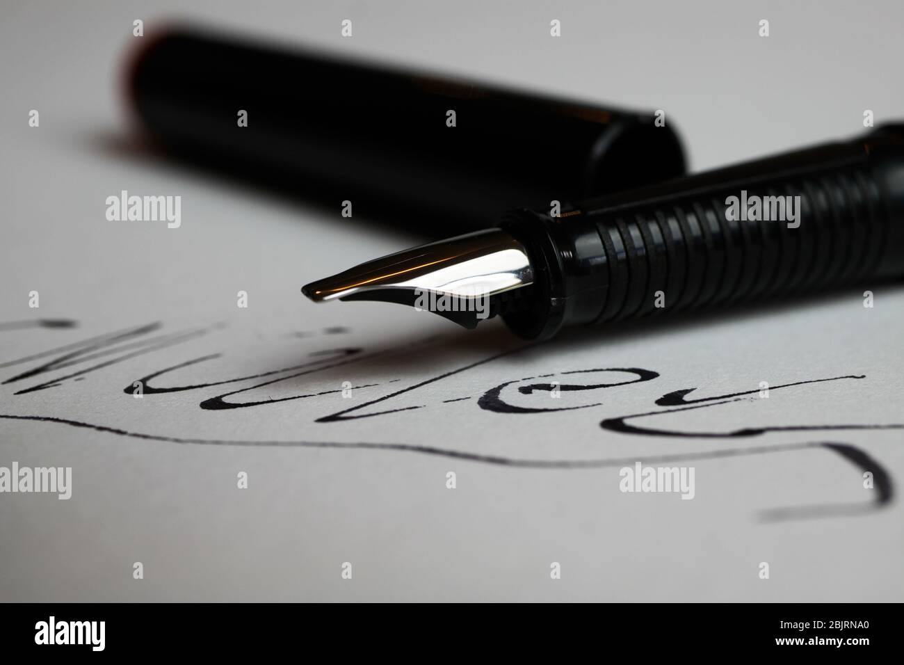 Contract conclusion concept: Macro close up of isolated black ink pen and handwritten signature on white paper (focus on tip of pencil) Stock Photo