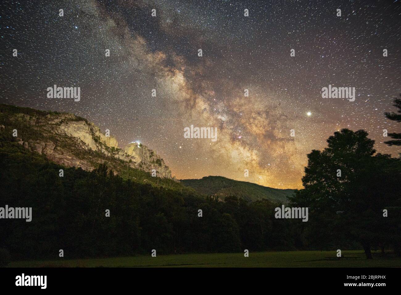 A group of climbers near the top of Seneca Rocks in West Virginia, as twilight ends and the Milky Way makes an appearance high above the mountains. Stock Photo