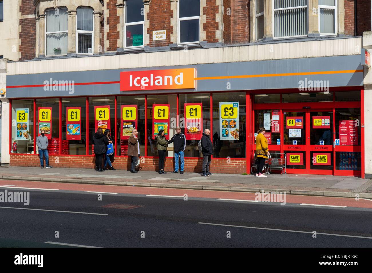 Shoppers performing social distancing while queuing outside an Iceland supermarket During the covid-19 pandemic Stock Photo