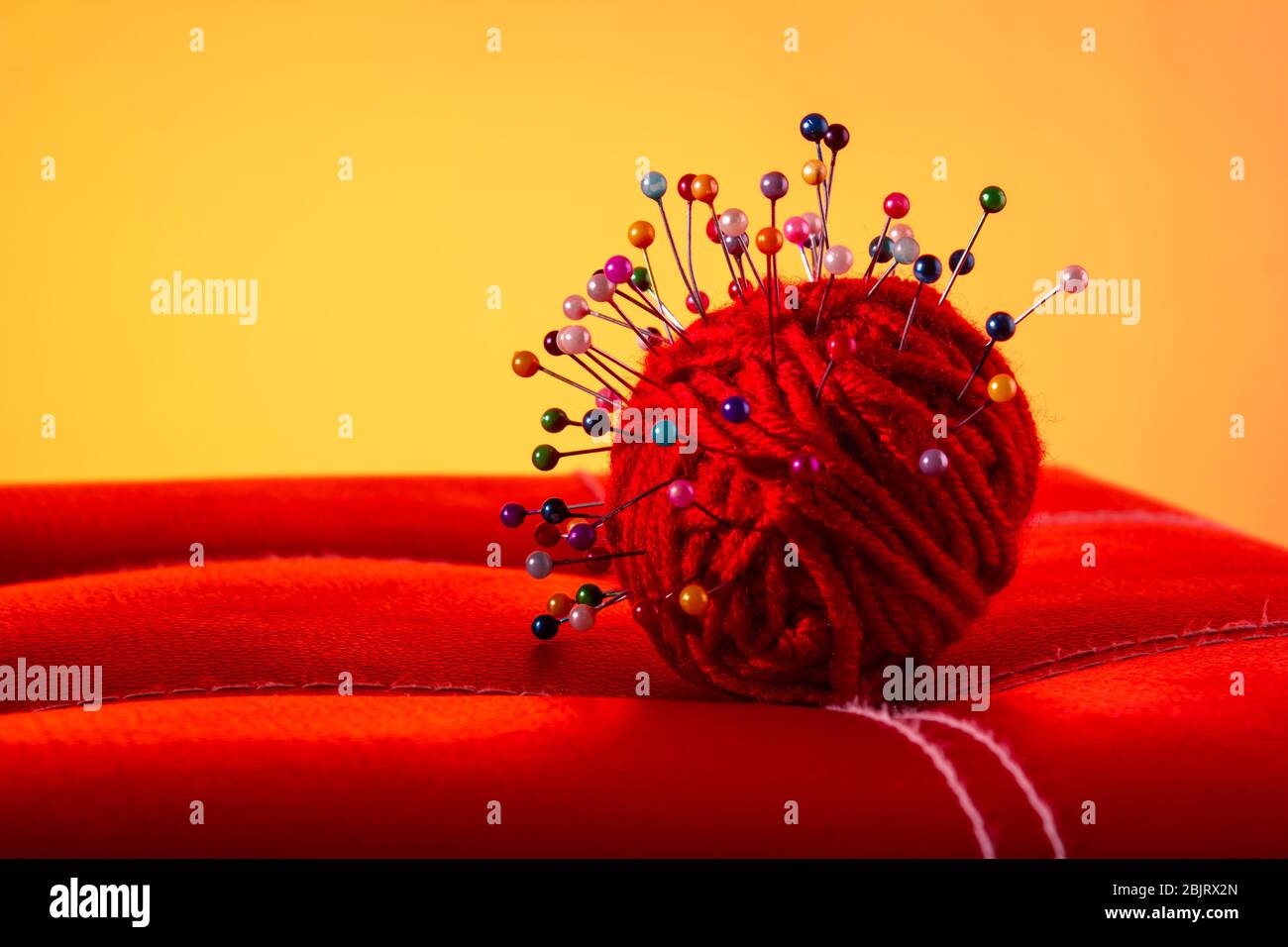 a red skein of thread stuck a lot of needles on red leather on an orange background. close up copy space Stock Photo