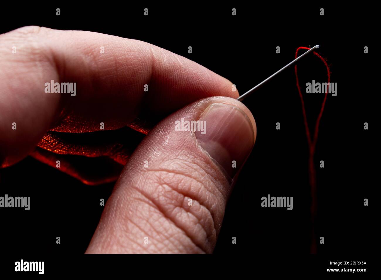 needle in hand with red thread on a black background Lush Lava backlight. close up copy space Stock Photo